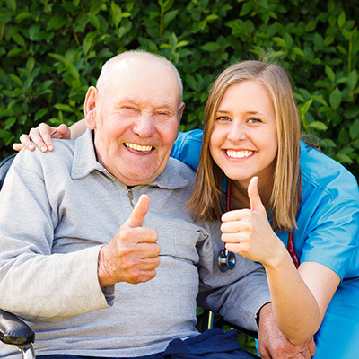 A senior and a nurse outside smiling holding up their thumbs.