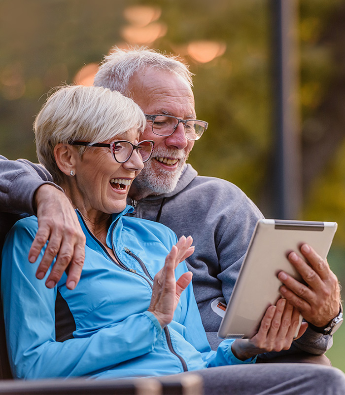 Two seniors on a tablet in a park setting.